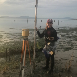 Julie Gonzalez with research equipment on marsh near water's edge.