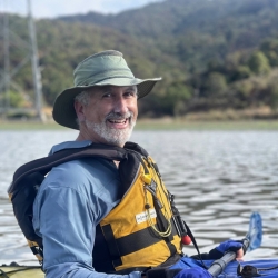 Stuart Siegel smiling in a kayak on the water wearing a fishing hat and yellow life vest